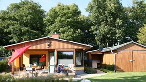 Et etplanshus med en overdækket terrasse, garage og græsplæne.