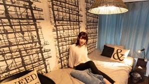 A bedroom with a bed, a wall with abstract patterns, a hanging light fixture, and a pillow with text. - RetroChaya1 (Osaka)