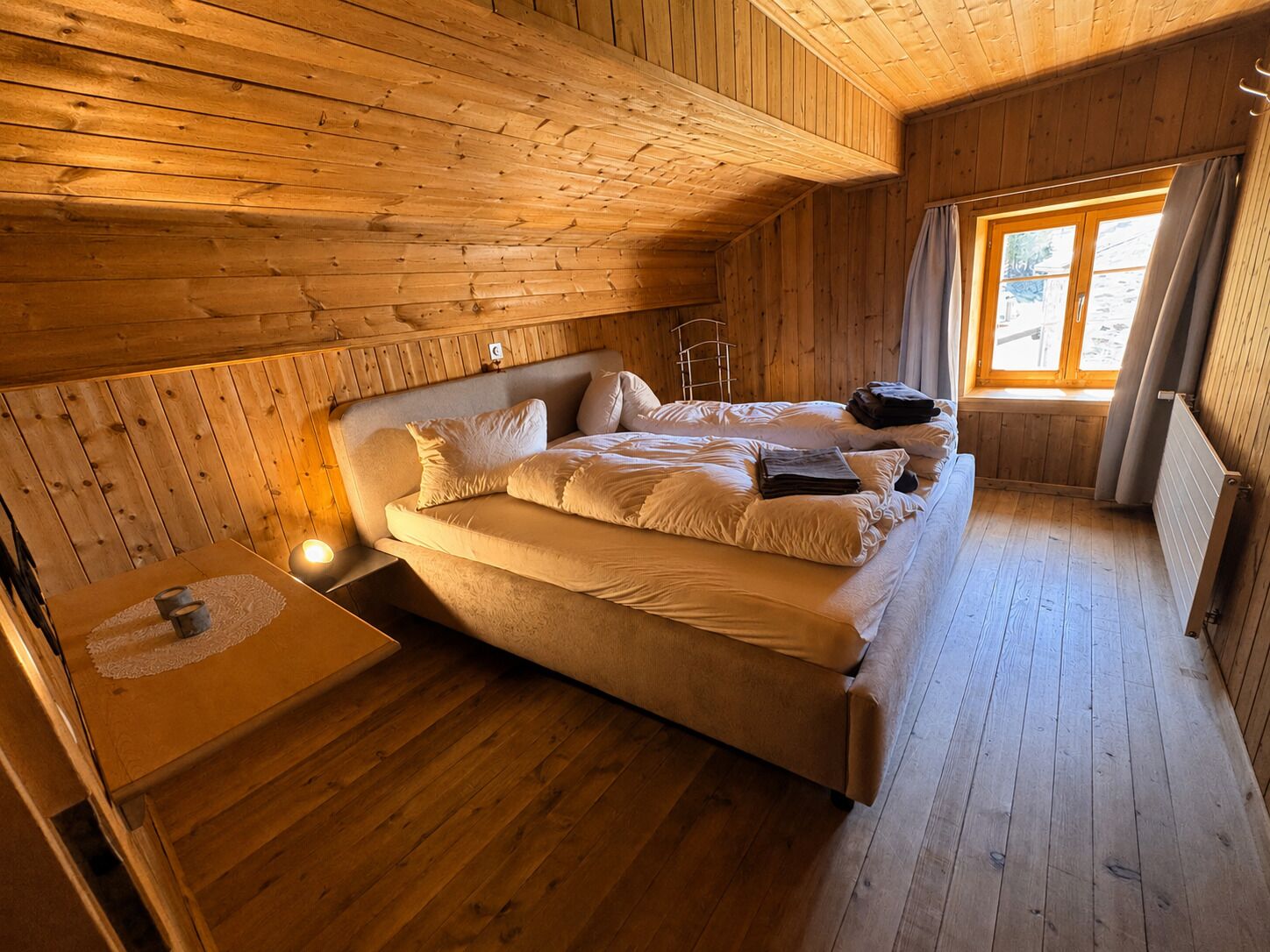 Ein Zimmer in einer Holzhütte mit einem Bett, einem kleinen Tisch und einem Fenster.
