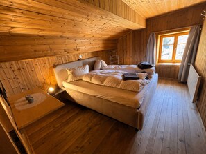 A wooden cabin room with a bed, a small table, and a window.
