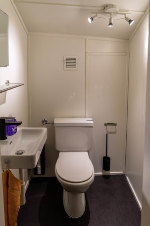 Ein kleines, weißes Badezimmer mit Toilette, Waschbecken und Spiegel. Ein Handtuch hängt an der Wand und ein schwarzer Teppich liegt auf dem Boden.