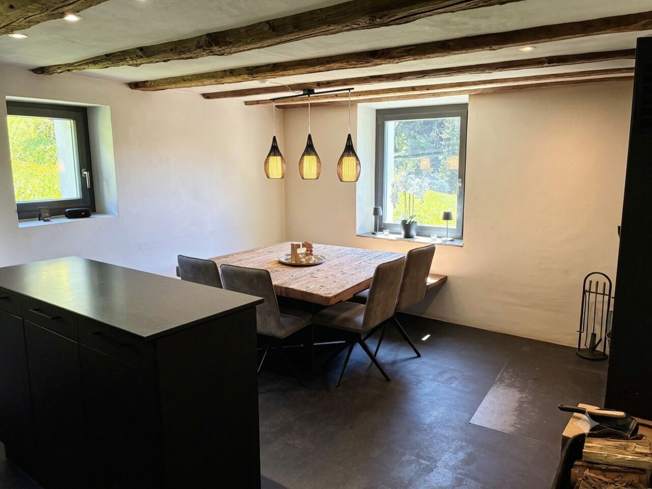 Un coin repas avec une table et des chaises en bois, des luminaires suspendus et une vue par la fenêtre.