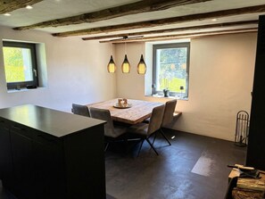 A dining area with a wooden table and chairs, pendant lights, and a view through a window.