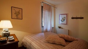 A bedroom with a bed, a bedside table with a lamp, a framed picture on the wall, and a window with curtains. - beautiful accommodation in a quiet location and with a huge garden, M2 (Pomaia)