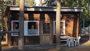 Een kleine houten hut met één deur en twee ramen, omringd door bomen.