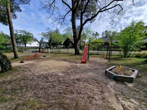 Un parque infantil con un sube y baja, un tobogán y columpios.