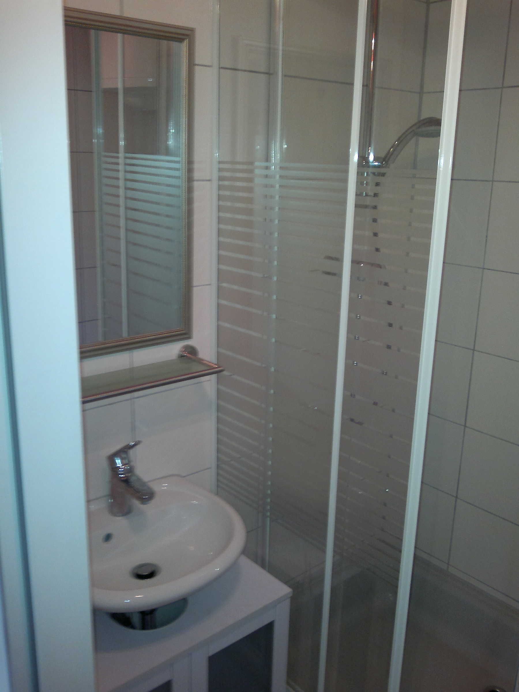 Une salle de bain avec un lavabo blanc, un miroir et une douche à parois de verre.