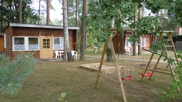 Eine Holzhütte mit Veranda, Schaukel und Spielbereich mit Spielzeug.