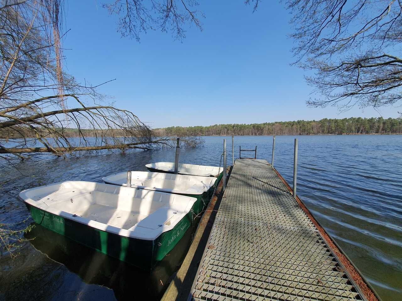 Een steiger met twee boten, een heldere lucht en een bebost oever.