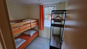 Une chambre de dortoir avec des lits superposés, une fenêtre avec des rideaux, un portant à vêtements et un sol carrelé.