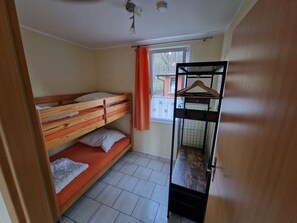 A dormitory room with bunk beds, a window with curtains, a hanging clothes rack, and a tiled floor.