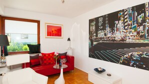Una sala de estar moderna con un sofá rojo, un sillón blanco, una mesa de centro de cristal y un cuadro abstracto grande en la pared.
