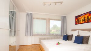 Un dormitorio con cama, ventana con cortinas, radiador y un cuadro en la pared.