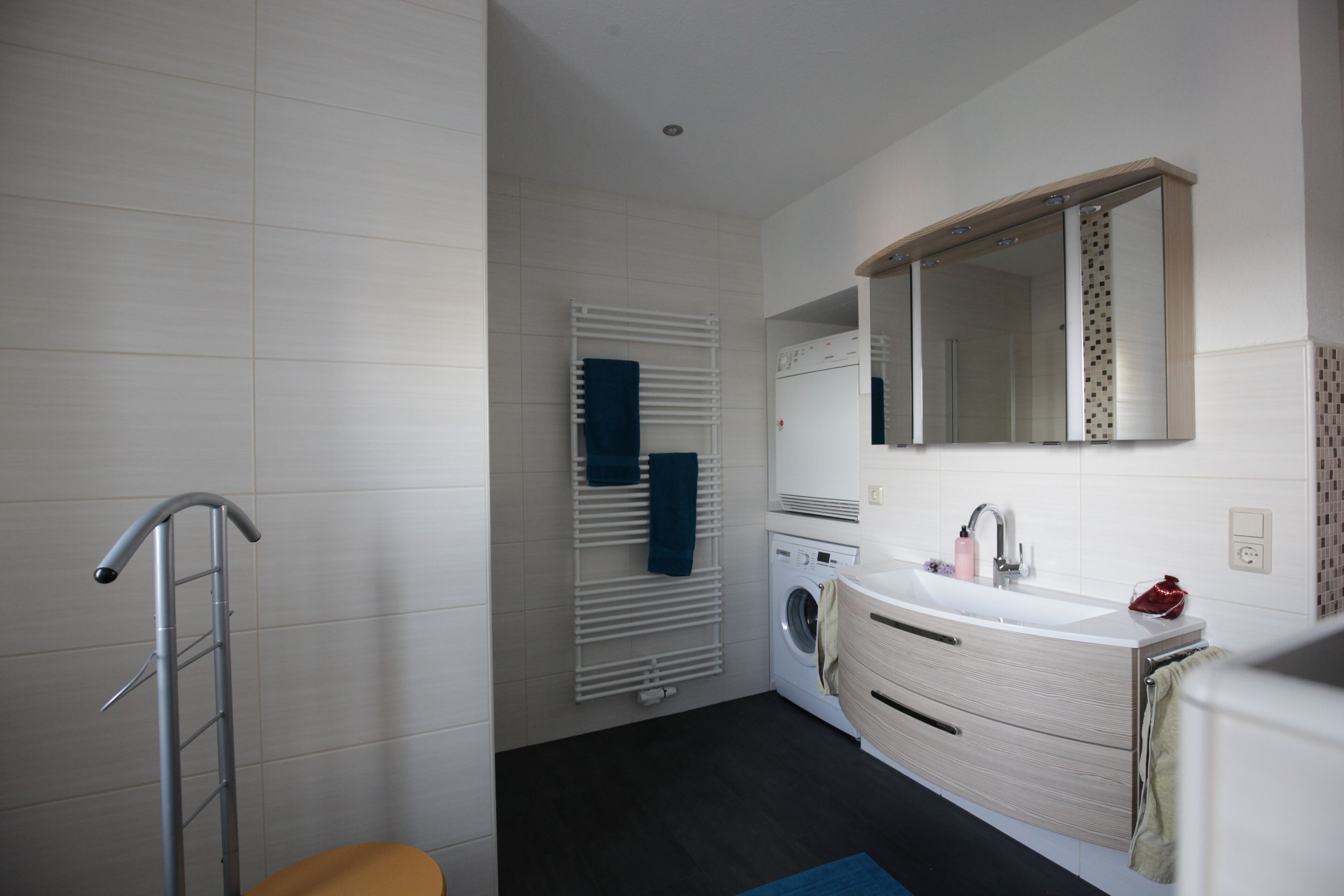 A modern bathroom with a built-in washing machine, a sink with a mirror above it, and a towel rack with towels.