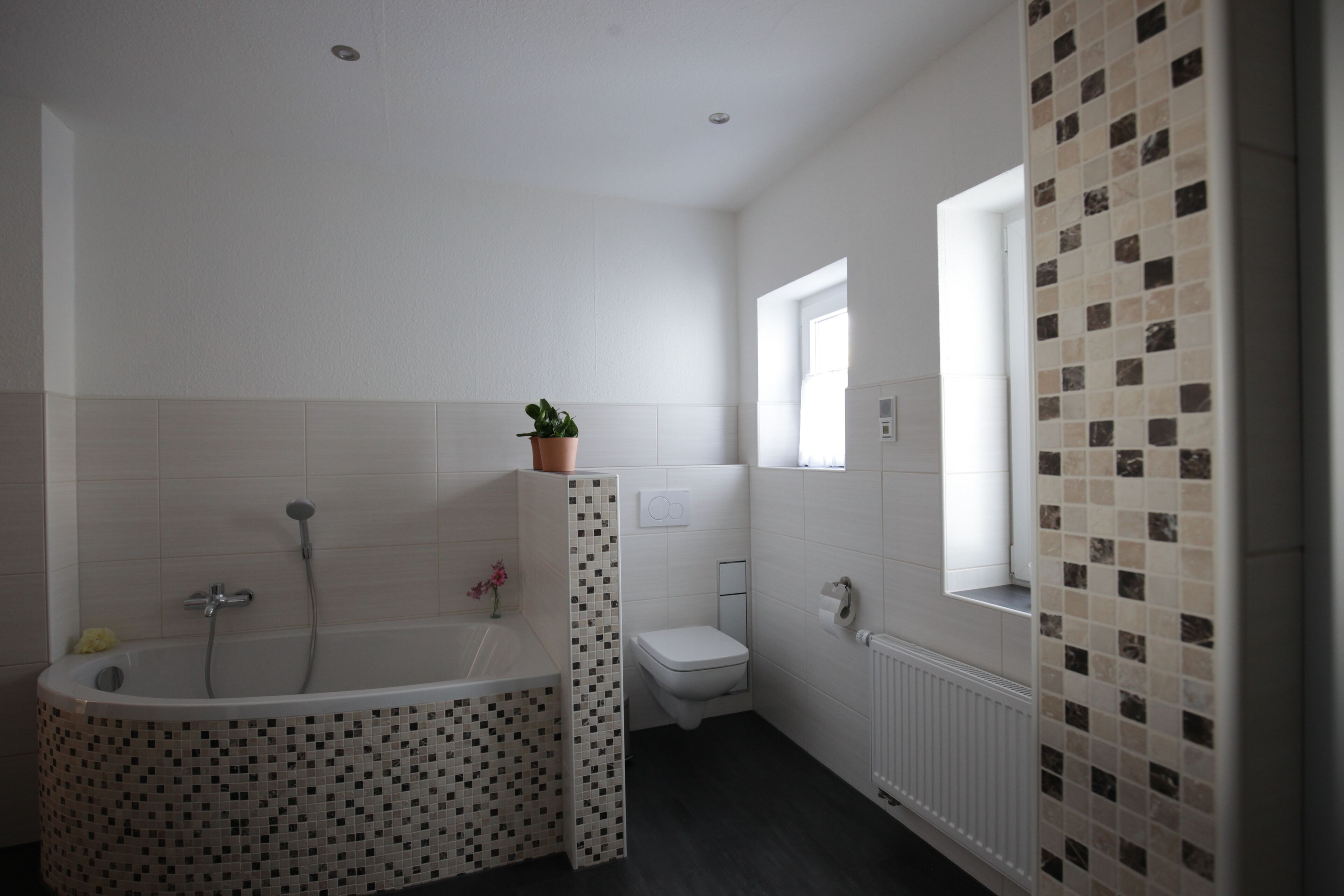 Et moderne badeværelse med et fristående badekar, toilet og et vindue der lukker naturligt lys ind.