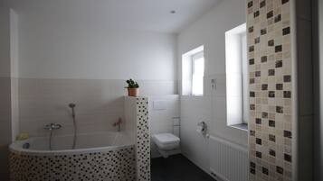 Et moderne badeværelse med et fristående badekar, toilet og et vindue der lukker naturligt lys ind.