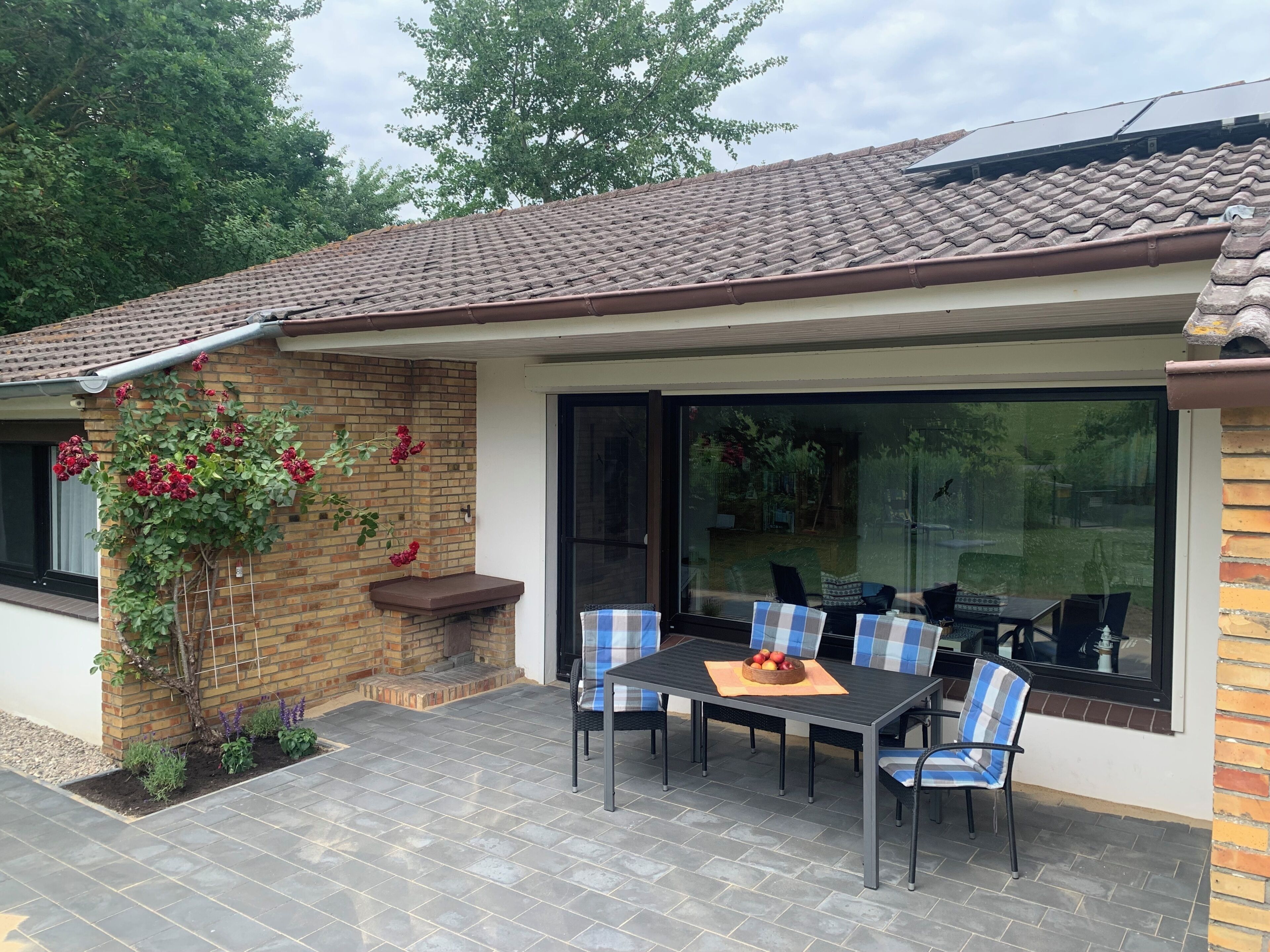 A patio with a table and chairs, a brick wall with climbing plants, and a glass door leading to a garden.