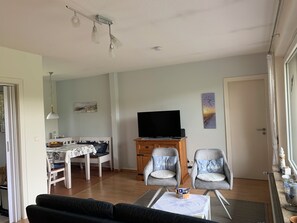 Un salon comprenant un canapé, deux fauteuils, un téléviseur et un coin repas avec une table et des chaises.