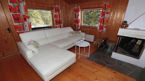A cozy room with a white sofa, two windows with red curtains, a small round table, and a fireplace. - BEAUTYFULL COTTAGE WITH MOTORBOAT and CANOE (Säffle)
