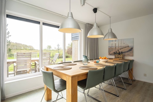A dining area with a wooden table, green chairs, and pendant lights.