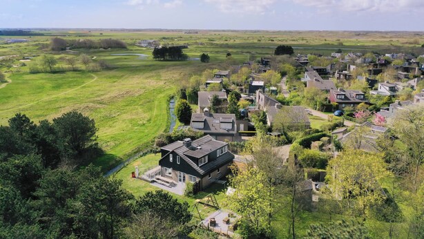 An aerial view of a residential area with houses, green fields, and a clear sky.