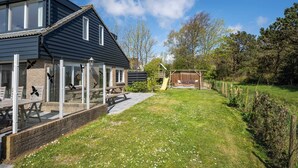 A modern house with a covered patio, a play area, and a well-maintained lawn.