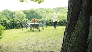 An outdoor seating area with a table and chairs, surrounded by greenery and a tree.
