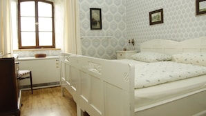 A room with a bed, a chair, a window, a radiator, and a wall with patterned wallpaper.
