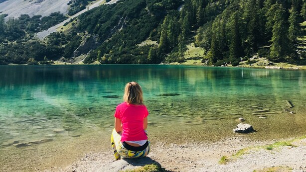 A person sitting by a lake with mountains in the background.