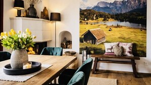 A dining area with a wooden table, chairs, a vase with flowers, and a large scenic wall mural.