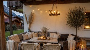 A cozy outdoor seating area with wicker furniture, a chandelier, and string lights.