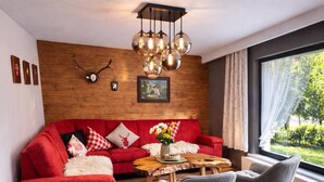 A modern living room with a red sofa, grey chairs, a wooden coffee table, and a large window with a view of greenery.