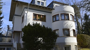 Une maison moderne à deux étages, dotée d’une façade incurvée, de grandes fenêtres et d’un escalier apparent menant à l’étage supérieur.