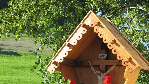 A wooden structure with a crucifix, surrounded by flowers and greenery. - Farm holidays Rotsteinhof (Vöran)