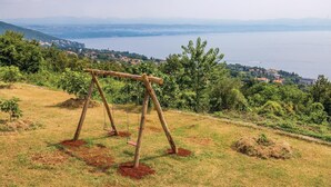 Ein hölzernes Schaukelgestell auf einer grasbewachsenen Anhöhe mit Blick auf eine Küstenstadt.