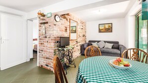 Ein Wohnzimmer mit Backsteinwand, einer Couch, einem Fernseher und einem Tisch mit kariertem Tischläufer.