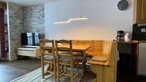 Ein kompakter Wohnraum mit Küchenzeile, einer Essecke mit Holzmöbeln, einem Flachbildfernseher und einer Wand mit Steinverkleidung.