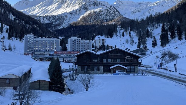Eine Berghütte mit Seilbahn, umgeben von schneebedeckten Bergen und Kiefern.