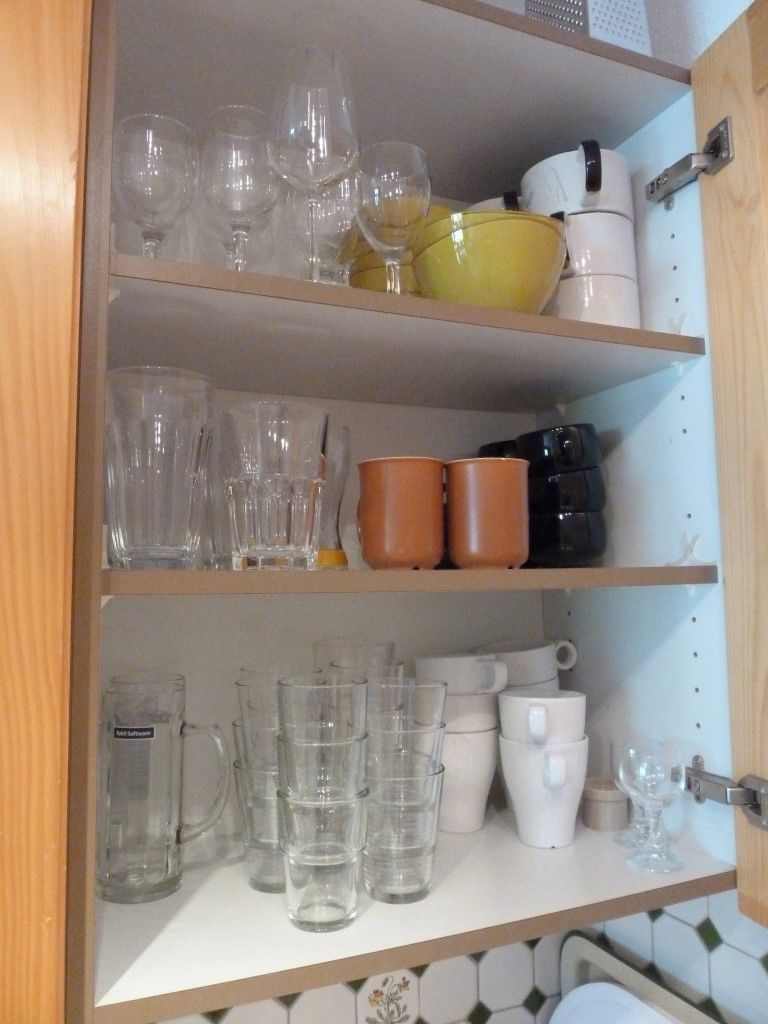 Un estante de cocina con diferentes vasos, incluyendo copas de vino y vasos tipo tumbler, además de tazas de cerámica.