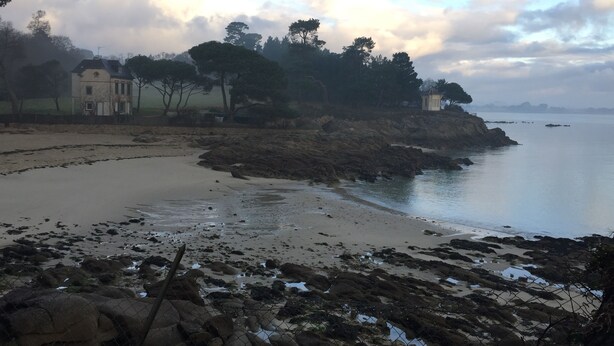 A coastal landscape with a sandy beach, rocky shoreline, and a building with a fence in the foreground. - Exclusively renovated farmhouse in southern Brittany (Fouesnant)