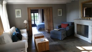 A living room with a white sofa, blue armchair, and a wooden coffee table. There is a fireplace and a bed in the background. - Exclusively renovated farmhouse in southern Brittany (Fouesnant)
