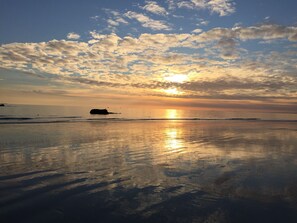 Une plage au coucher du soleil, avec une mer calme et un ciel dégagé.