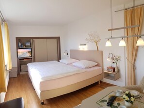 A hotel room with a bed, bedside table, lamp, and a small table with a vase and flowers. - Apartment "Strandgut" - Apartment Strandgut (Karlshagen)