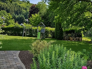 A garden with a swing set, a small playhouse, and a brick pathway.
