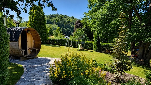 A garden with a wooden barrel sauna, a children's play area, and a paved walkway.