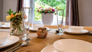 A dining table set with plates, glasses, and cutlery, with a window view of greenery and a flower vase.