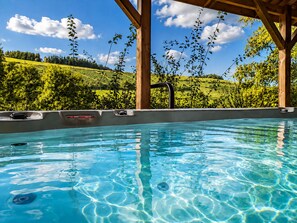 A clear blue pool with wooden beams overhead, surrounded by lush greenery and a clear sky.