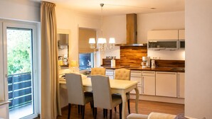 A modern kitchen with a dining area, a TV, and a view of greenery outside.