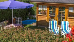 A wooden gazebo with a pool, surrounded by lush greenery and a patio with a table and chairs. - Apartment A (2-3) - Apartments and Bed & Breakfast Eberle (Jungholz)
