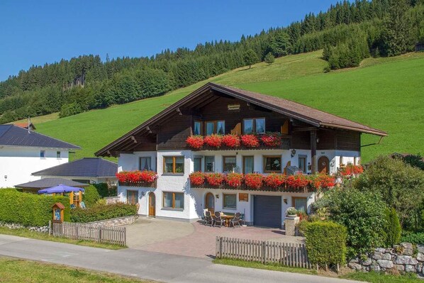 A two-story building with a sloped roof, multiple windows, and flower boxes on the balconies. - Apartment A (2-3) - Apartments and Bed & Breakfast Eberle (Jungholz)